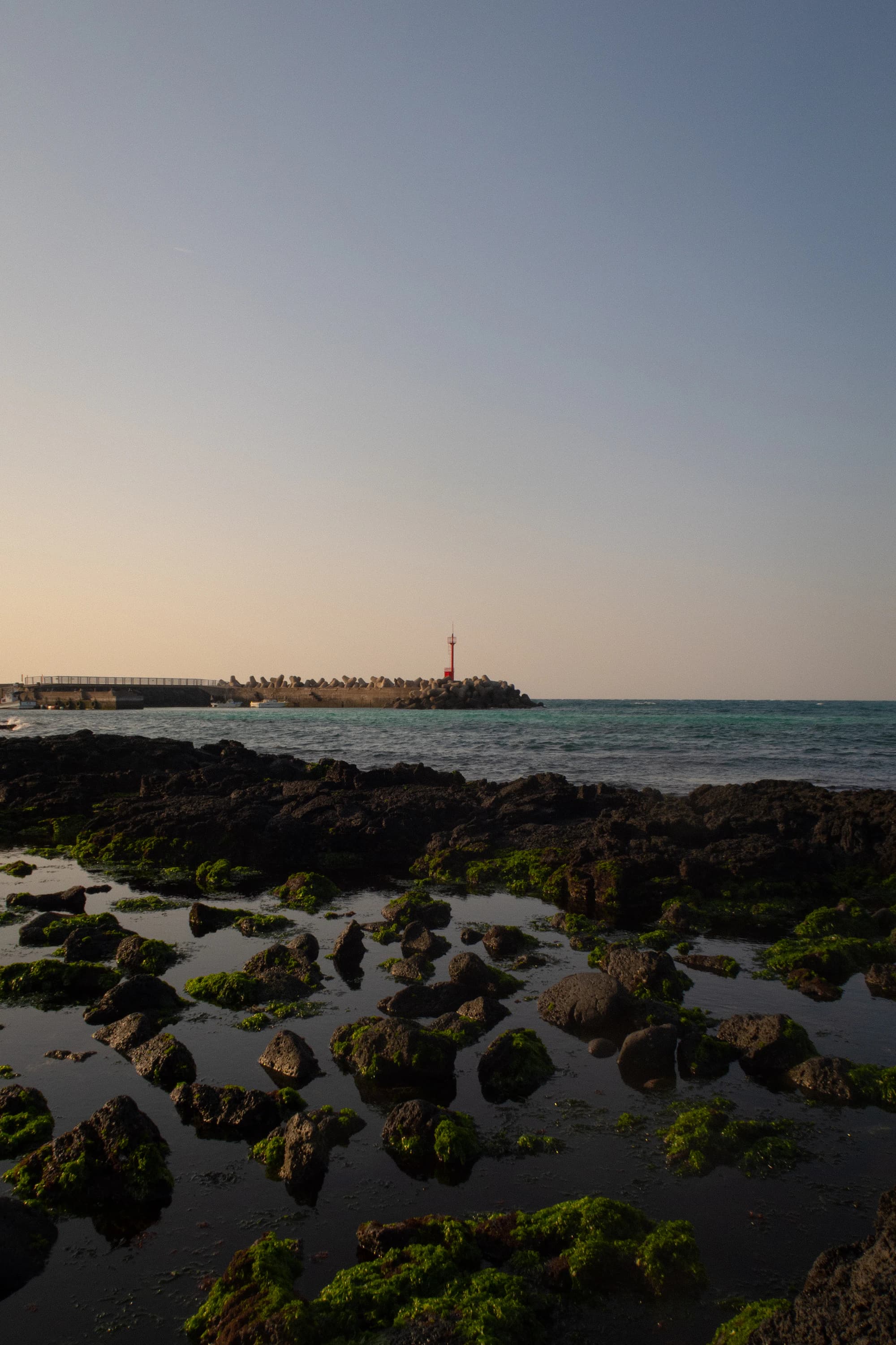 Pyoseon-area lighthouse at sunset over basalt tide pools