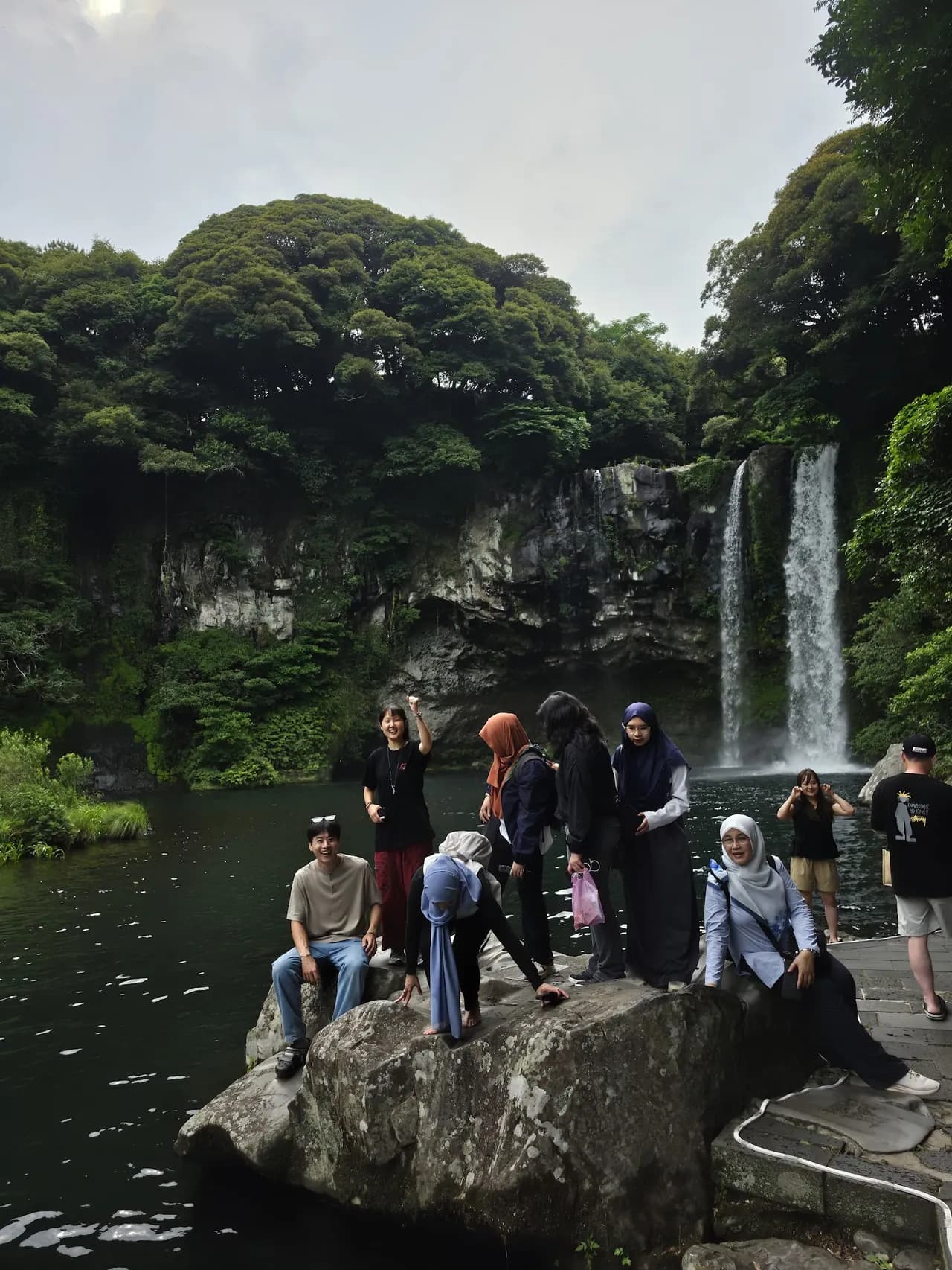 Guests on the rocks beside a Jeju waterfall pool