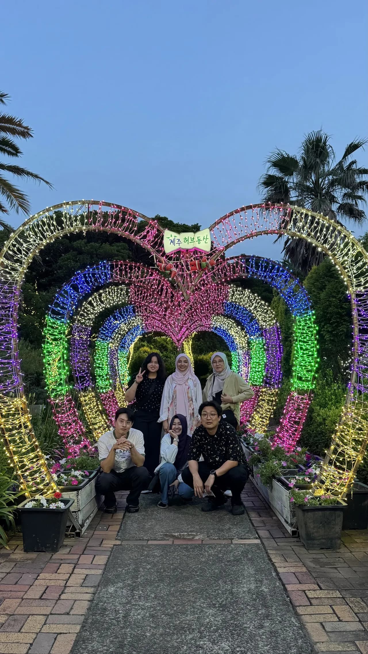 The group under a glowing neon arch at a night light garden